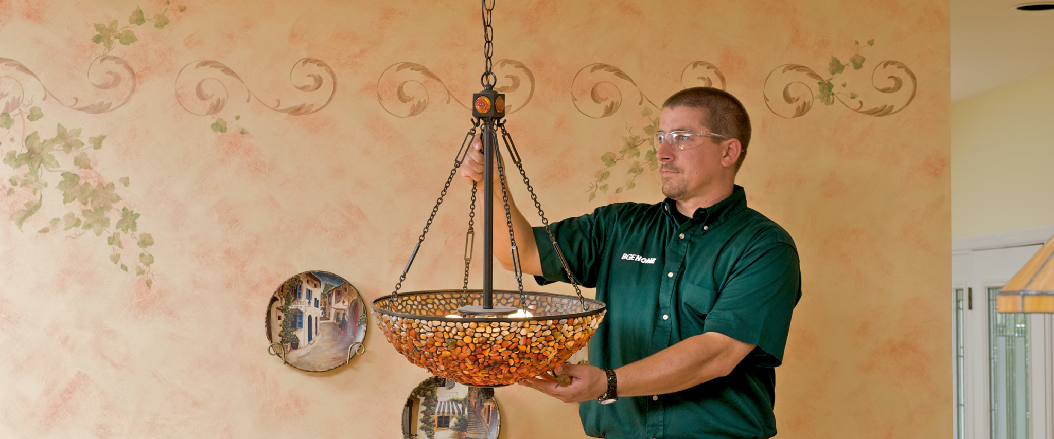 An electrician hangs a light fixture in a home