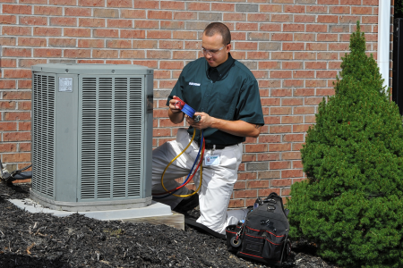 an HVAC technician is working on a HVAC condensing unit box outside a home.